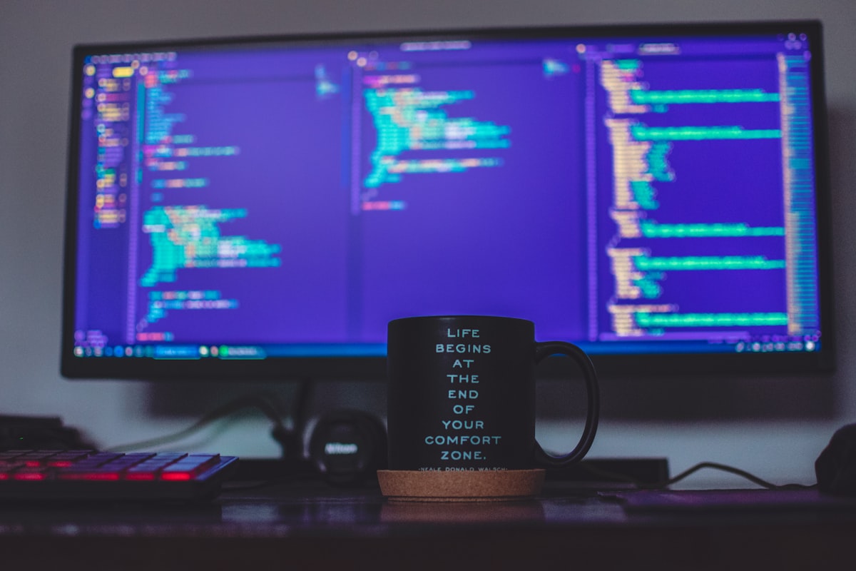 A monitor and coffee mug on a dark desk